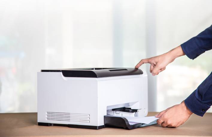 An employee carefully retrieves legal documents from a scanner in a professional environment on a sunny day.