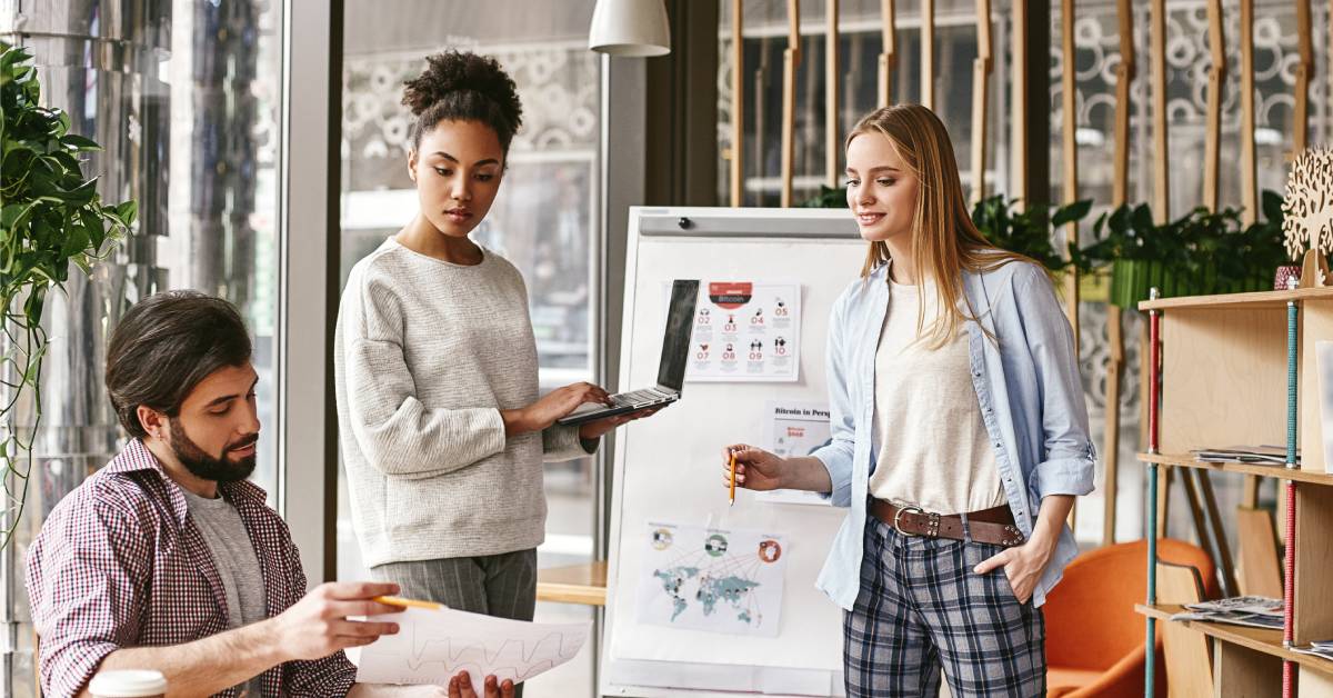 An employee is sitting and holding a piece of paper while two other employees are standing and looking at the paper.