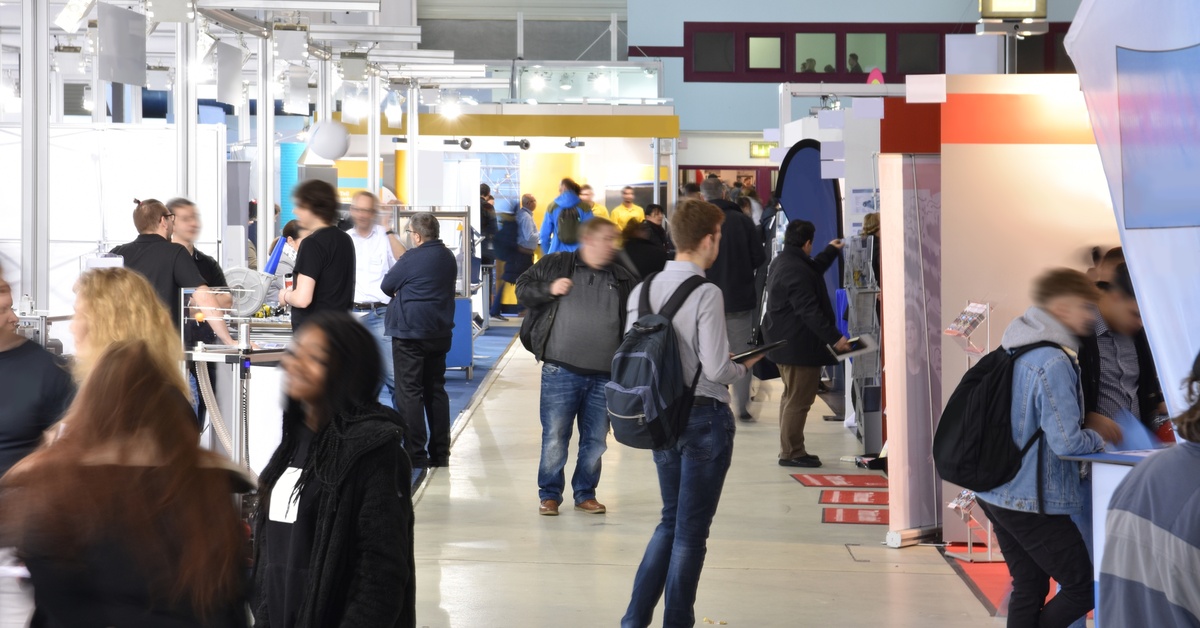 A busy trade show in a modern convention center, with many people walking around to each business booth.