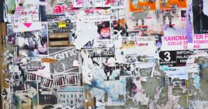 A gray concrete wall covered by multiple posters, all featuring different graphics, colors, and sizes.