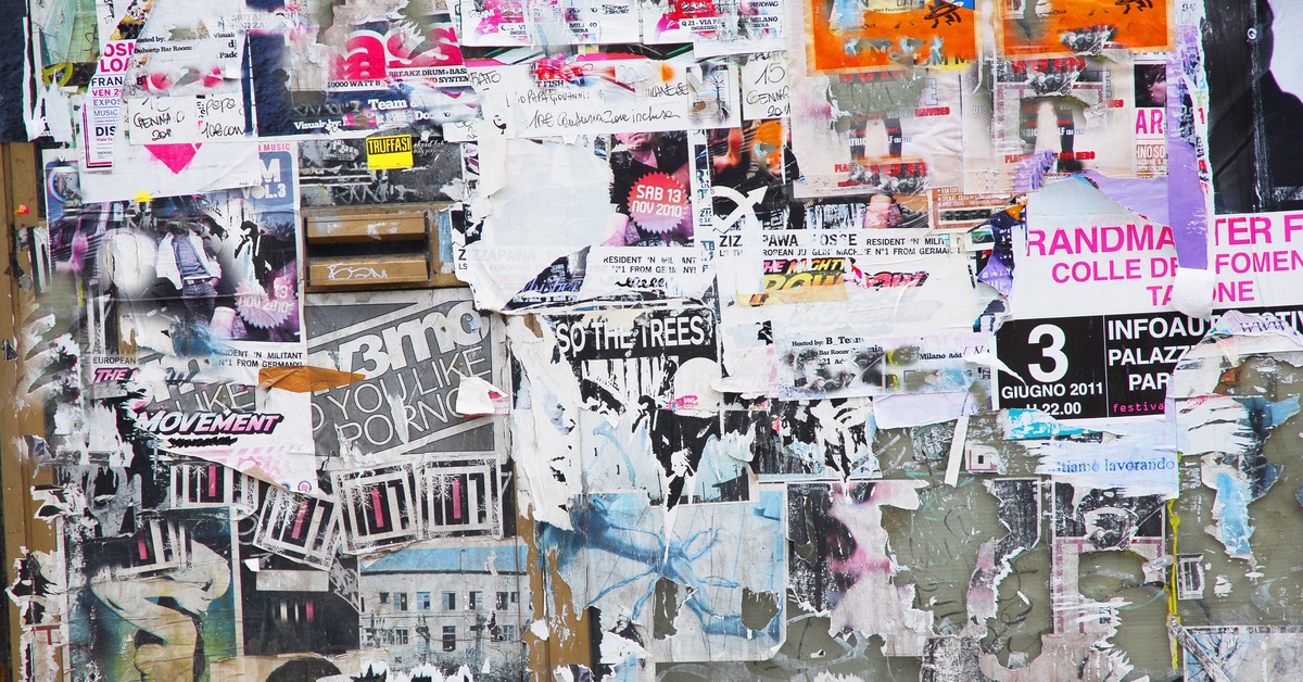 A gray concrete wall covered by multiple posters, all featuring different graphics, colors, and sizes.