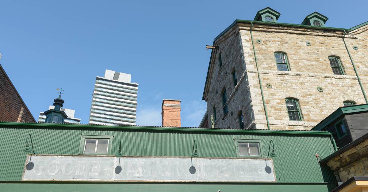 A green building with an old, faded storefront business sign on a distillery. The letters can hardly be seen.