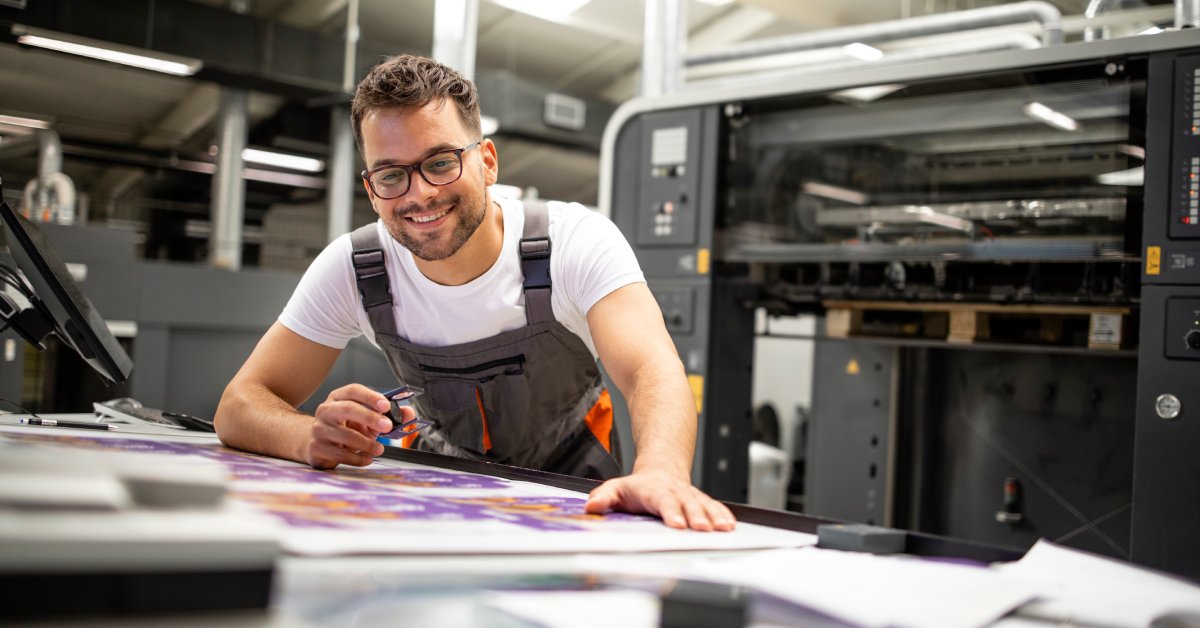 A mean wearing a gray apron and white shirt smiles while looking down at a professionally printed poster.
