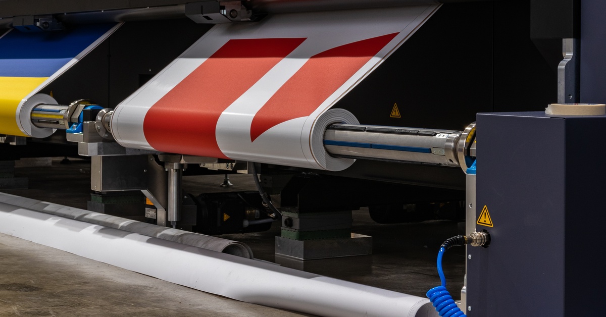 An industrial printer produces a white banner with bold red stripes as the material rolls through the print system.