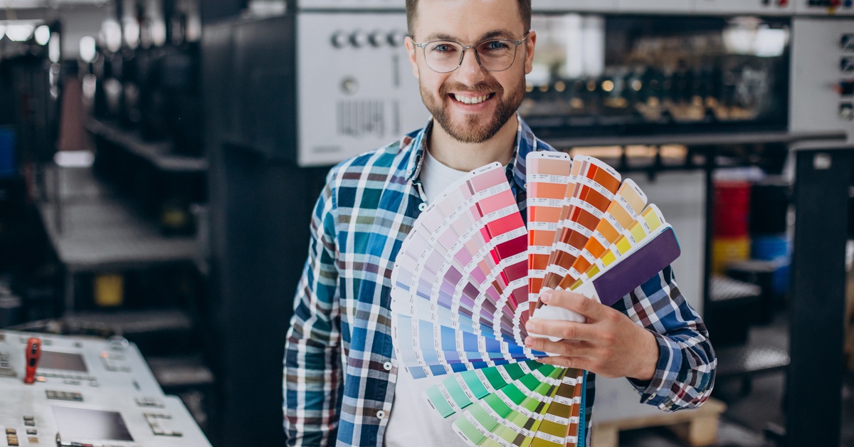 A printing professional displays multiple color palette fans while standing in a print production facility.