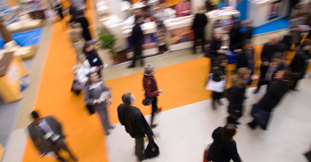 Attendees move through a busy trade show floor as colorful aisles and exhibition booths fill the convention hall.